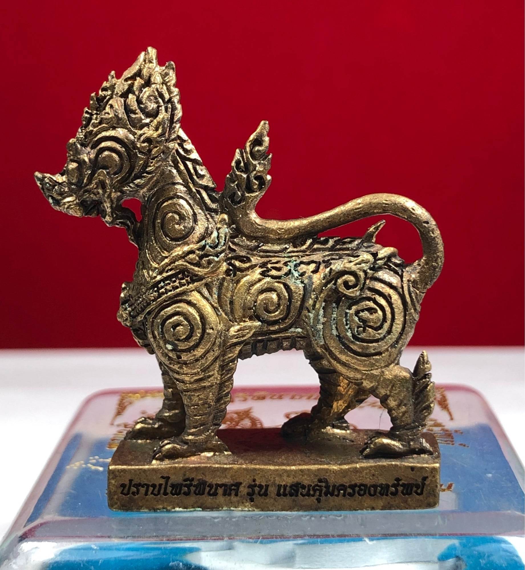 Gold tone Singha Guardian Amulet figurine with ornate spiral carvings on a rectangular base with Thai script