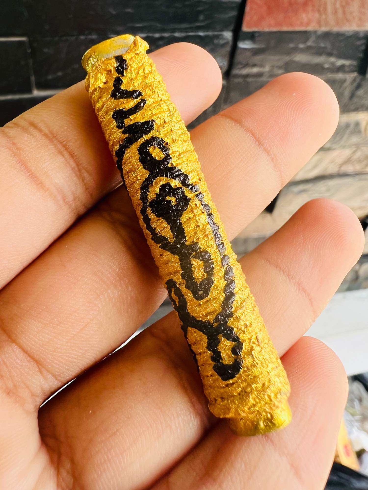 Hand holding gold cylinder amulet with black sacred script by Thai Blessing Co authentic Thai spiritual amulets for protection