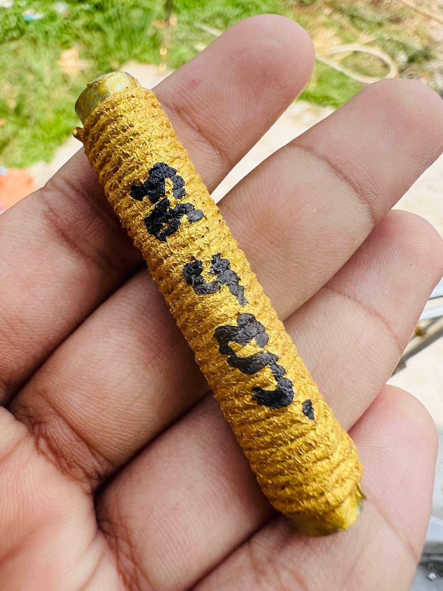Handheld yellow threaded takrut amulet with black script on brass ends from Thai Blessing Co authentic Thai spiritual amulets