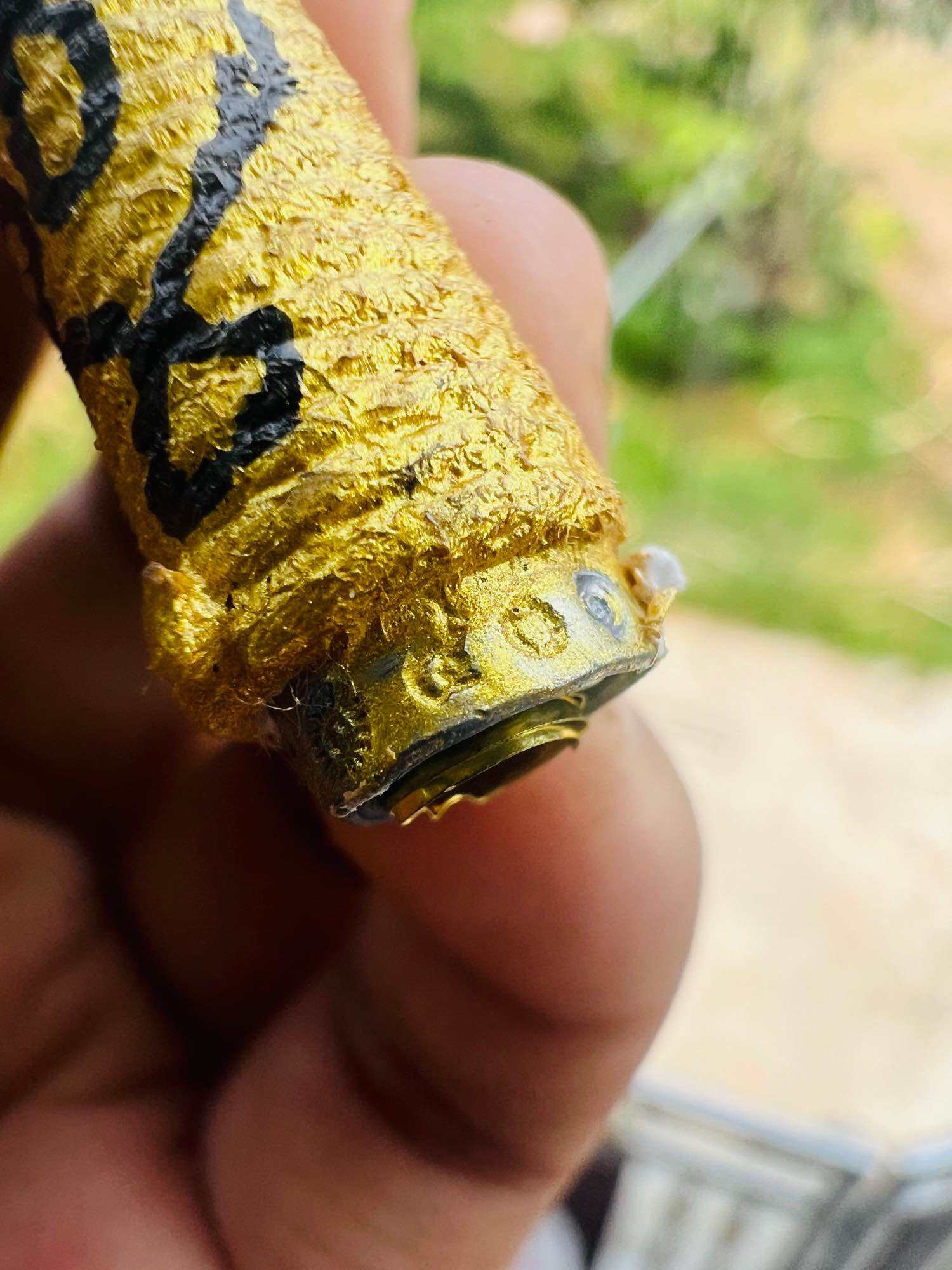 Close up of hand holding small gold foil wrapped amulet with black script and metal cap authentic Thai spiritual amulets