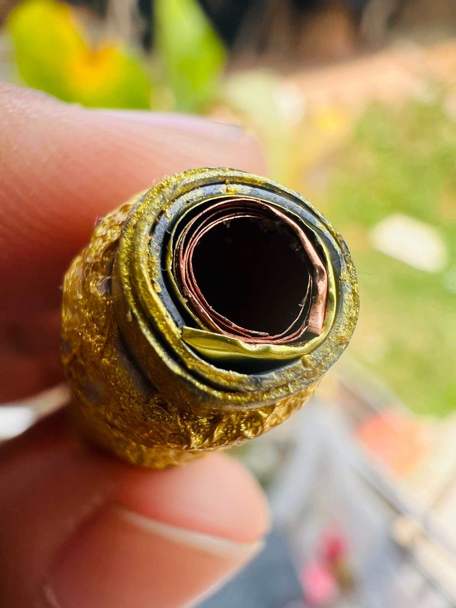 Close up of gold wrapped Thai amulet pendant with rolled metal core held by fingers authentic Thai spiritual amulets