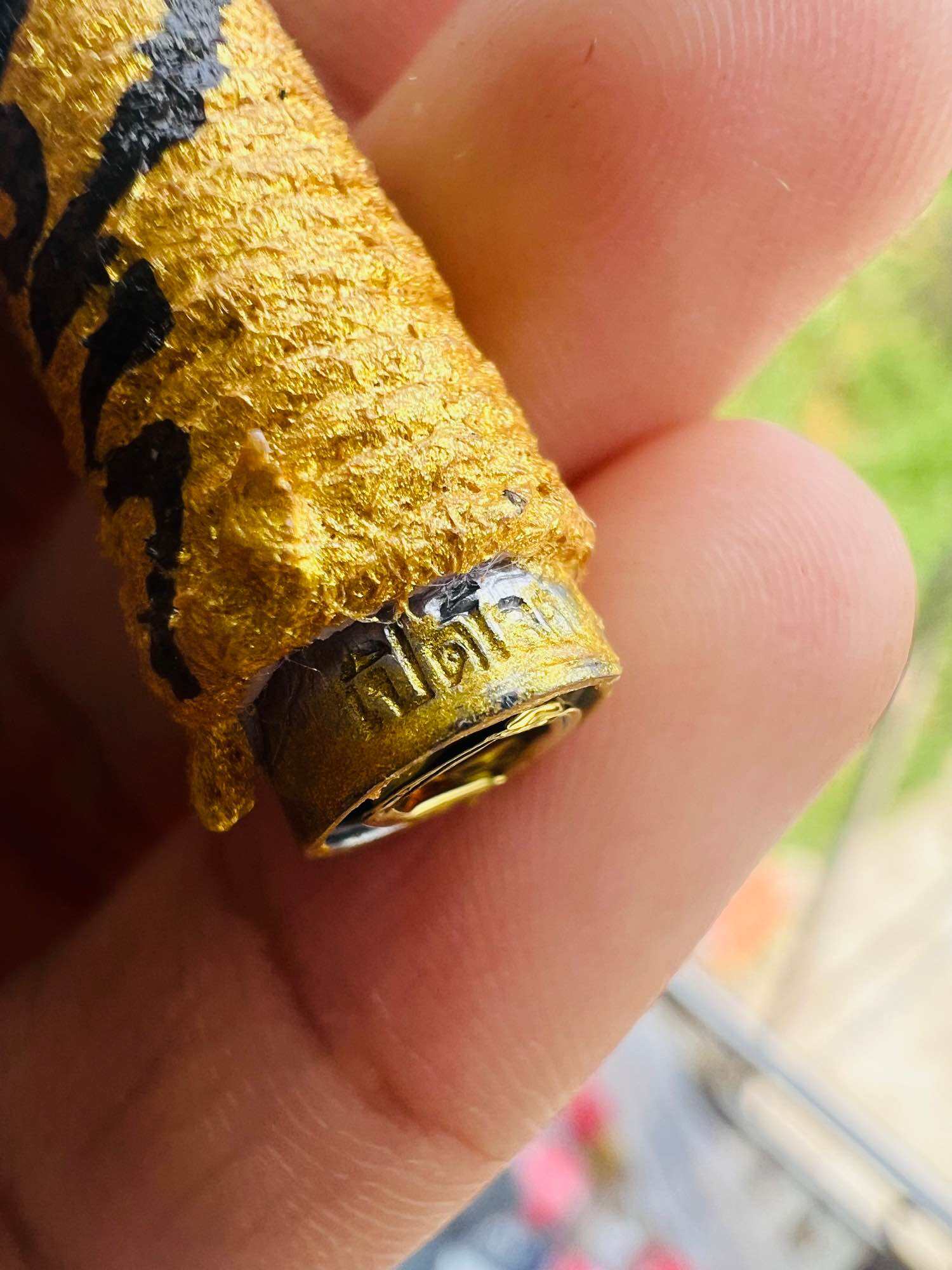 Hand holding authentic Thai spiritual amulets wrapped in gold cloth with metal cap and Thai script