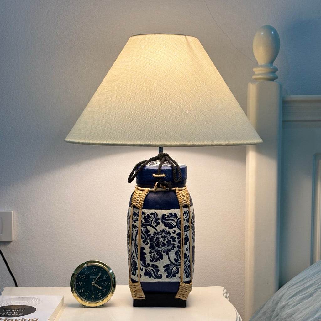Woven bamboo rice basket lamp with blue floral pattern and cream lampshade on bedside table