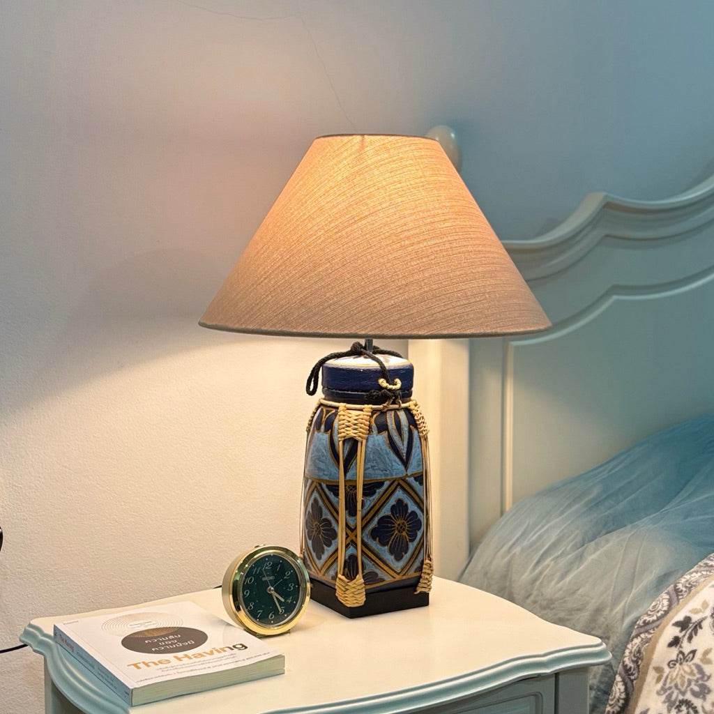 Woven bamboo rice basket lamp with fabric shade on a bedside table next to a clock and book