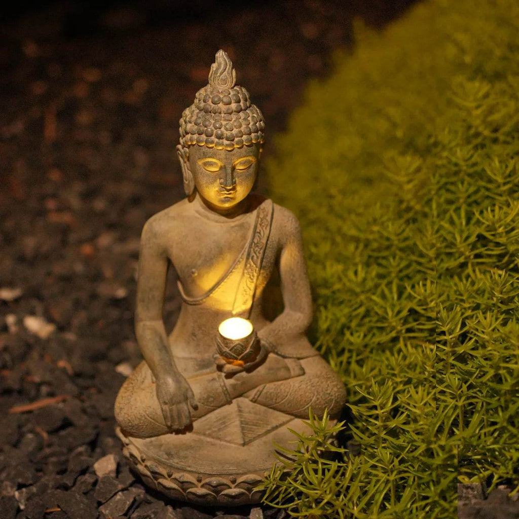 Thai Blessing Co solar powered Buddha garden statue glowing at night seated on gravel beside green moss for serene outdoor decor