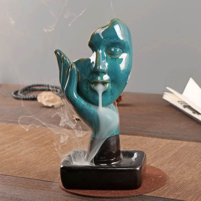 Teal ceramic face backflow incense burner for home with cascading smoke on wooden table decorative sculpture
