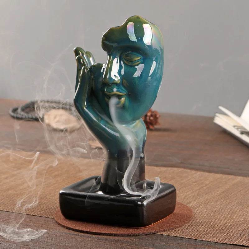 Teal ceramic sculpted face backflow incense burner for home with cascading smoke waterfall on table