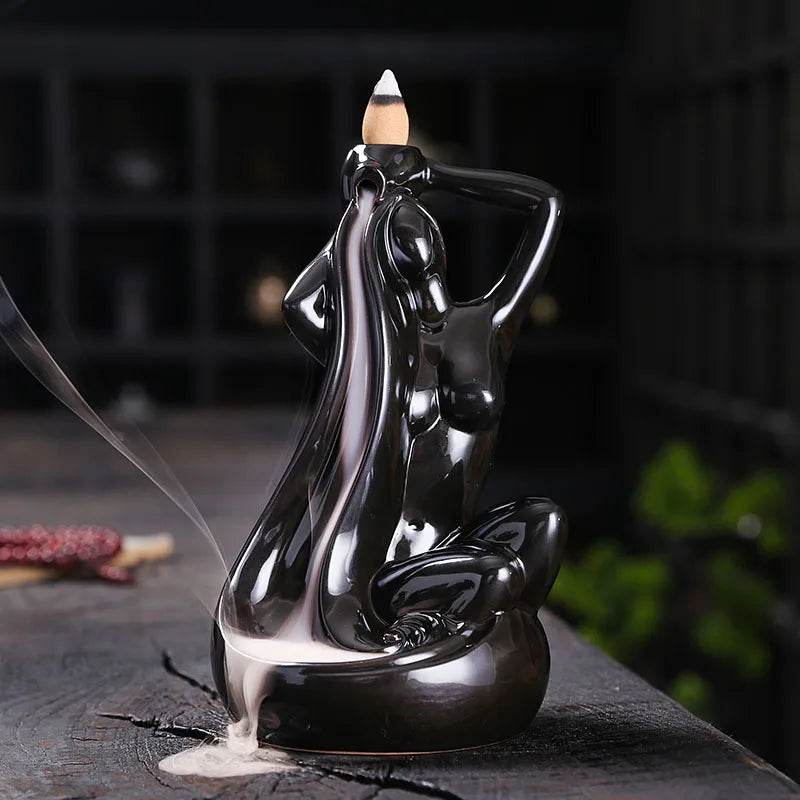 Glossy black ceramic backflow incense burner shaped as a seated woman with flowing hair and cascading smoke